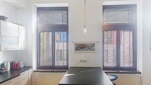 Une cuisine avec deux fenêtres, un radiateur, un plan de travail noir et une chaise.