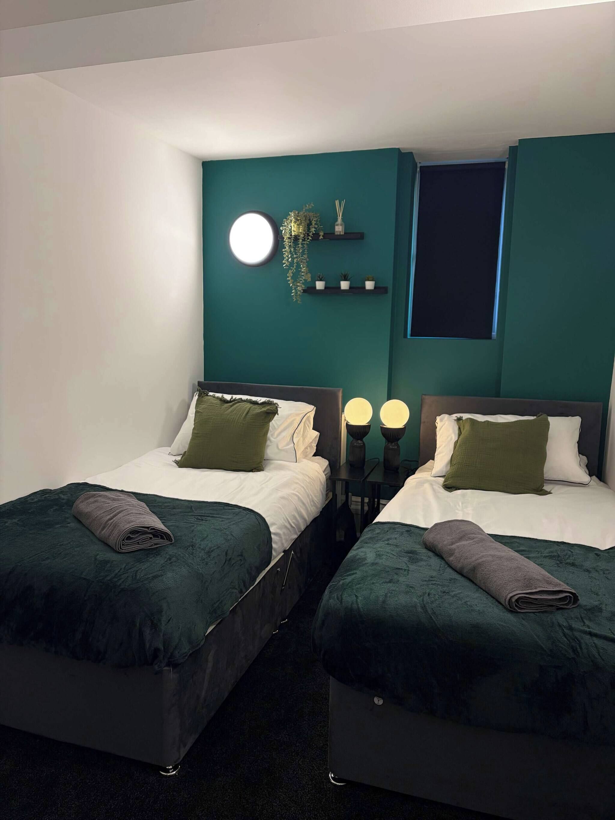 A room with two beds, a round wall clock, and a window.