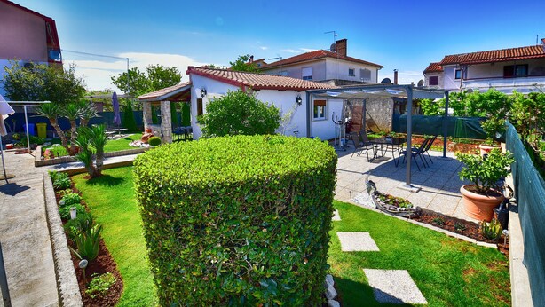 Zona residenziale con un giardino curato, un patio con mobili da esterno e un edificio bianco con tetto in tegole rosse.