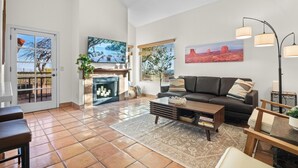 Een ruime woonkamer met een open haard, een bank, een salontafel en een eethoek met stoelen.