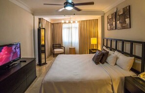Ein Hotelzimmer mit einem Bett, einem Fernseher, einem Sessel, einer Lampe und einem Deckenventilator.