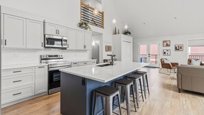 A modern kitchen with white cabinetry, a central island with stools, a built-in oven, and a microwave.