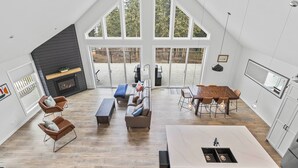 A spacious loft with a high ceiling, a fireplace, a dining area, and large windows.