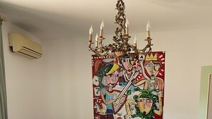 Een eethoek met een ronde tafel, witte stoelen, een groene bank en een kleurrijk abstract schilderij aan de muur.