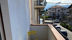 Een balkon met gele stoelen en een tafel, met uitzicht op een straat met geparkeerde auto's en gebouwen.