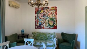 Een woonkamer met een groene bank, een witte tafel, een kroonluchter en een groot abstract schilderij aan de muur.