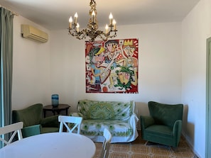 A living room with a green sofa, a white table, a chandelier, and a large abstract painting on the wall. - Villa Linda Casa Grande x 9 (Giardini Naxos)