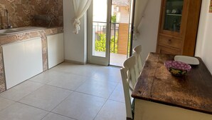 Een keuken met een betegelde spatwand, een houten tafel met een kom, en een glazen schuifdeur die leidt naar een balkon.