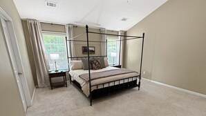 Una cama con dosel en un dormitorio con piso alfombrado, dos mesitas de noche y una ventana con cortinas.