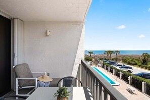 Ein Balkon mit Blick auf den Strand, einen Pool und geparkte Autos.