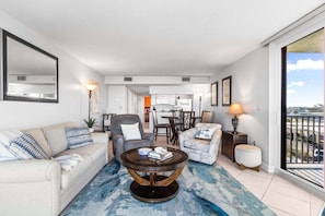 Ein Wohnzimmer mit einer Couch, Sesseln, einem Couchtisch und einem Essbereich im Hintergrund.
