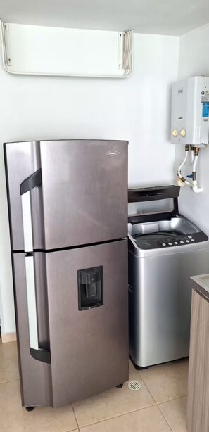 Une cuisine compacte équipée d’un réfrigérateur en acier inoxydable, d’un four encastré et d’un chauffe-eau.