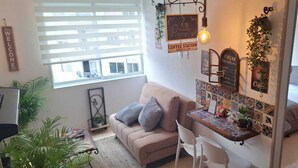 Una habitación acogedora con sofá, una mesita con espacio para café, cama y ventana con persianas.