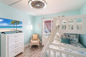 A bedroom with a bunk bed, a desk, a chair, and a television displaying a beach scene. - Anna Maria Island Club Unit 38 (Bradenton Beach)