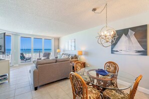 A spacious living area with a balcony overlooking the sea, a dining table with chairs, and a chandelier. - Anna Maria Island Club Unit 38 (Bradenton Beach)