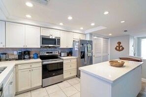 A modern kitchen with white cabinetry, stainless steel appliances, and a central island. - Anna Maria Island Club Unit 38 (Bradenton Beach)