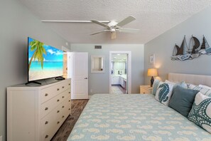 Ein Schlafzimmer mit einem Bett, einem Fernseher, einem Deckenventilator, einer Kommode und einer Tür zu einem Badezimmer.