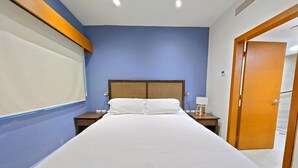 Een hotelkamer met een bed, nachtkastje, lamp en een deur.