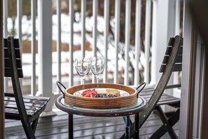 A wooden table with a glass bowl containing food and two glasses of water, set on a porch with a railing. - Parkside Downtown Retreat | Walkable (Traverse City)