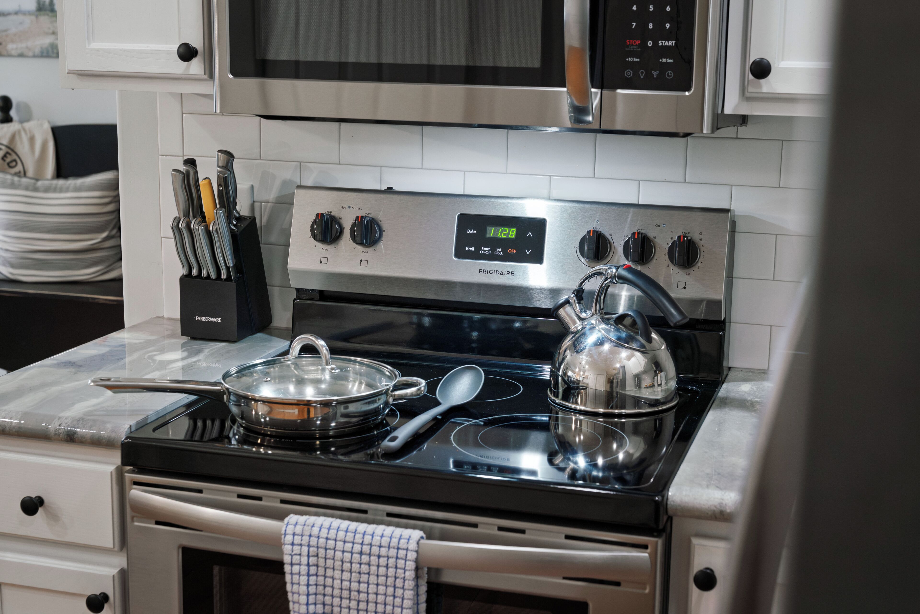 Una cocina con estufa de acero inoxidable, un microondas encima y un juego de cuchillos en un soporte.
