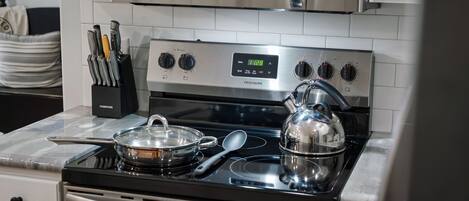 Una cocina con estufa de acero inoxidable, un microondas encima y un juego de cuchillos en un soporte.