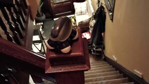 A wooden staircase with a metal railing, a red trash bin, and a hat on the railing.