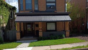 A two-story brick house with a front porch, a small garden, and a gravel driveway.