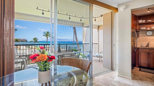Ein Balkon mit Glastisch, Korbstühlen und einem Blumentopf mit Blumen.
