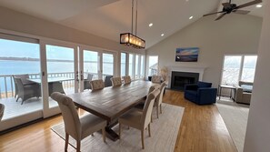 Un comedor amplio con una gran mesa de madera y sillas, una chimenea y vistas al agua.