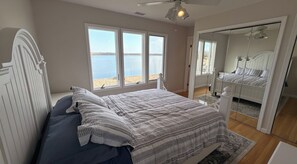 A bedroom with a bed, a large window with a view of the water, a ceiling fan, and a mirror. - Open Bayfront!  4-bedroom house tranquil Bayfront home minutes from Shinnecock! (East Quogue)