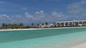 Een strand met helder turquoise water, wit zand en een rij witte gebouwen in de verte.