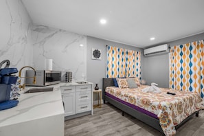 A modern bedroom with a bed, bedside table, and a desk with a microwave. - Retreat for Two: Spa Bath & King Suite in Montrose (Houston)