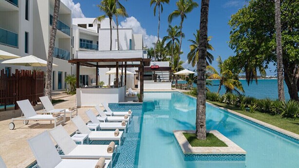Zona de piscina con sillones de descanso, un espacio de estar cubierto y vista al océano.