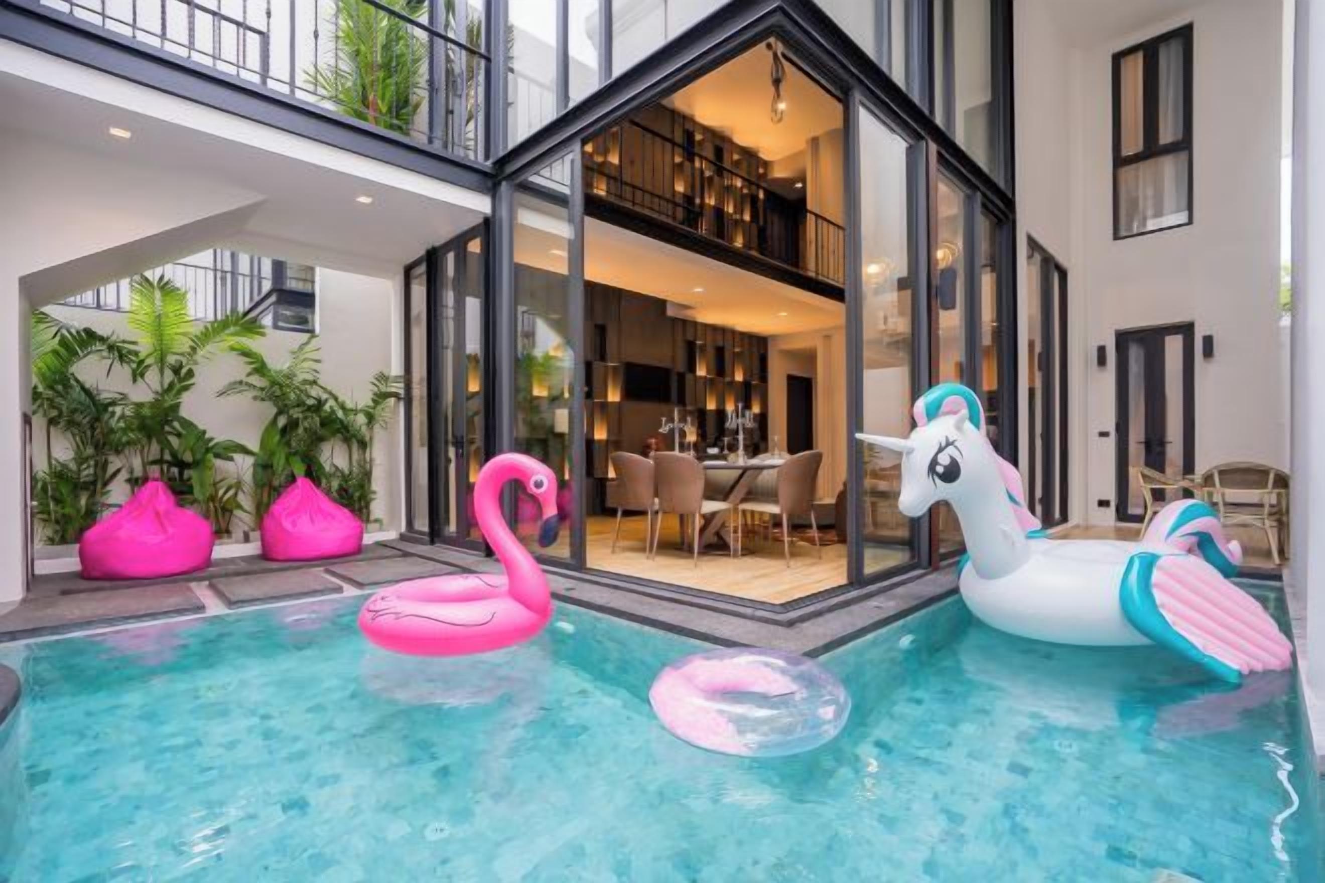 An indoor swimming pool with inflatable flamingo and unicorn floats, surrounded by modern architecture and indoor plants.
