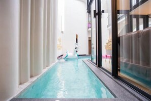 A narrow indoor swimming pool with a swan float, glass walls, and a modern interior design. - Moon 5-Bedroom Luxury Pool Villa (Pattaya)