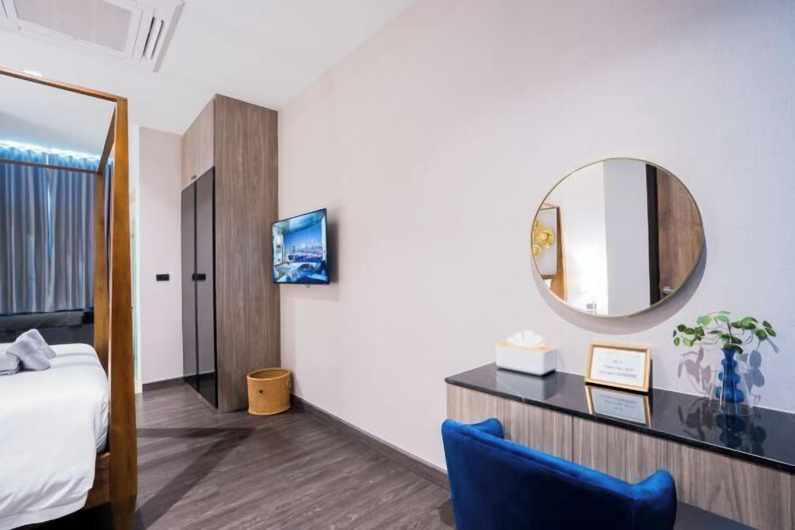 A hotel room with a bed, a desk with a mirror, a television, and a plant.