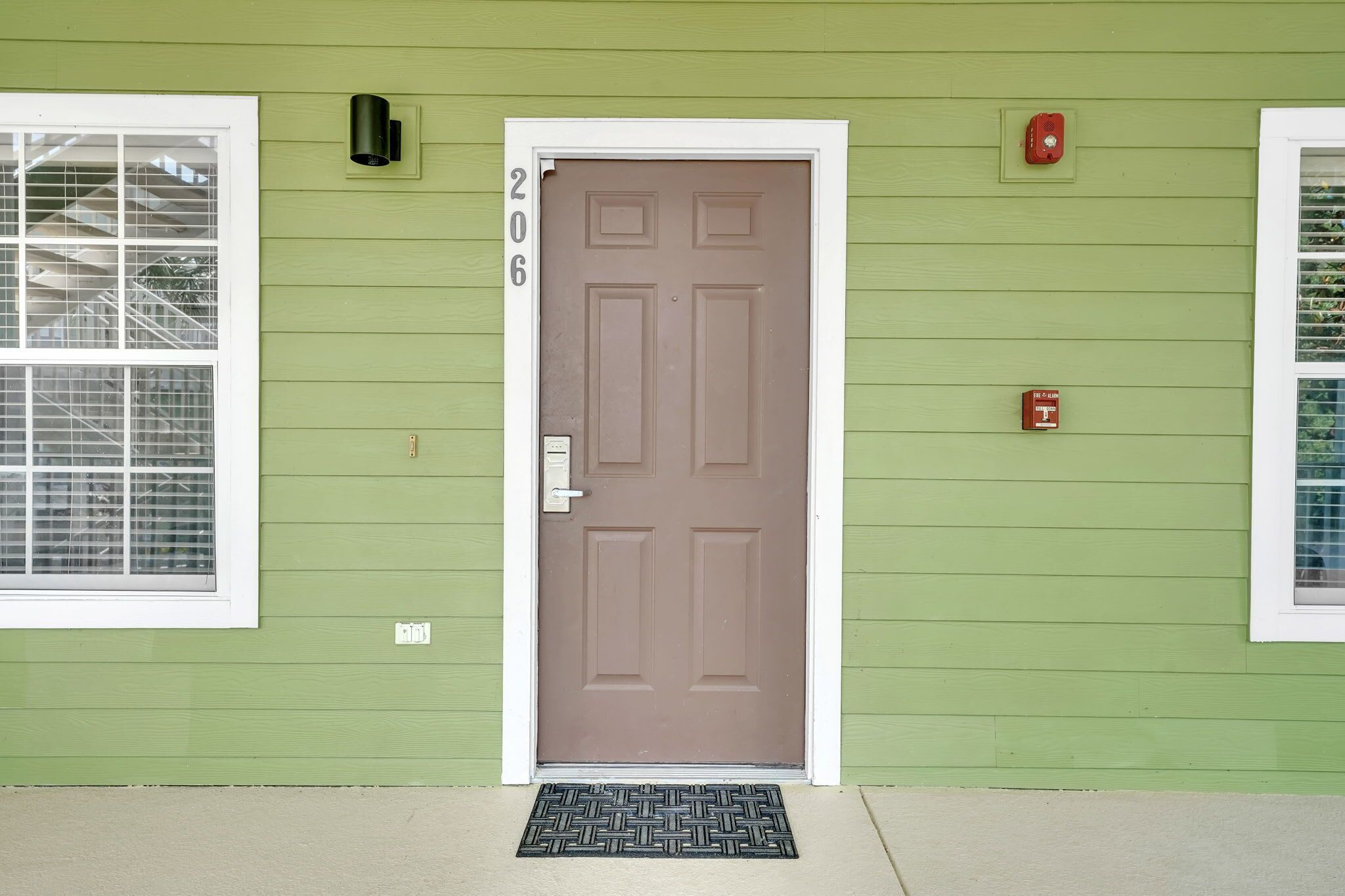 A green house with a brown door, a window with a metal grill, and a number '206' on the wall.