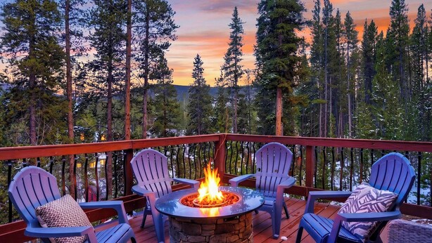 Une terrasse dotée d’un foyer en pierre, entourée de fauteuils Adirondack, et offrant une vue sur une zone boisée.