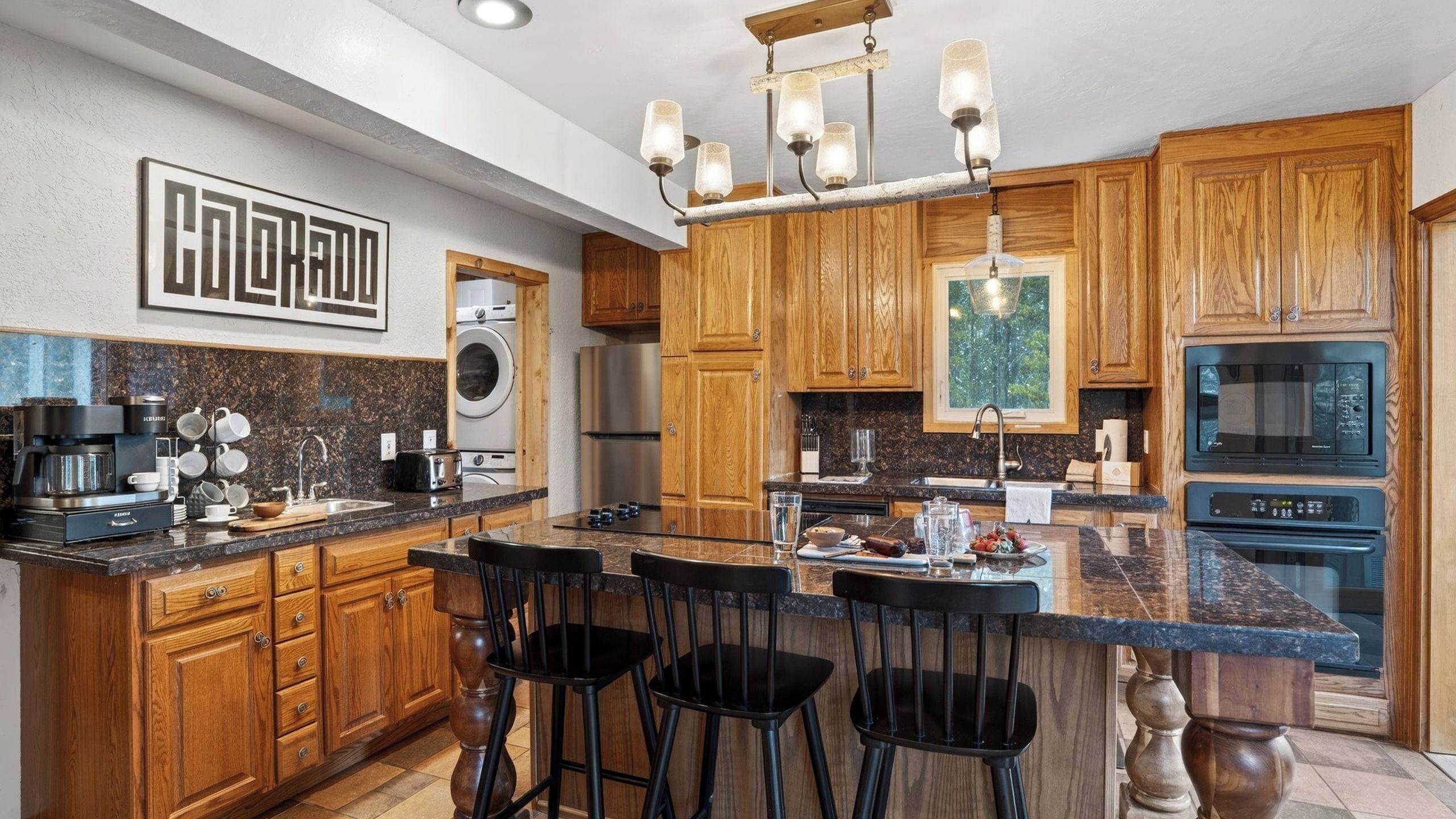 A kitchen with wooden cabinets, a central island with bar stools, a coffee maker, and a microwave.