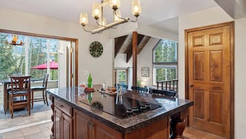 A kitchen with a large island, wooden cabinetry, a chandelier, and large windows offering a view of trees.