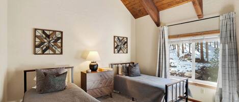 A bedroom with two beds, a nightstand, a lamp, and a window with a view of a snowy landscape.