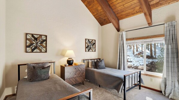 A bedroom with two beds, a nightstand, a lamp, and a window with a view of a snowy landscape.