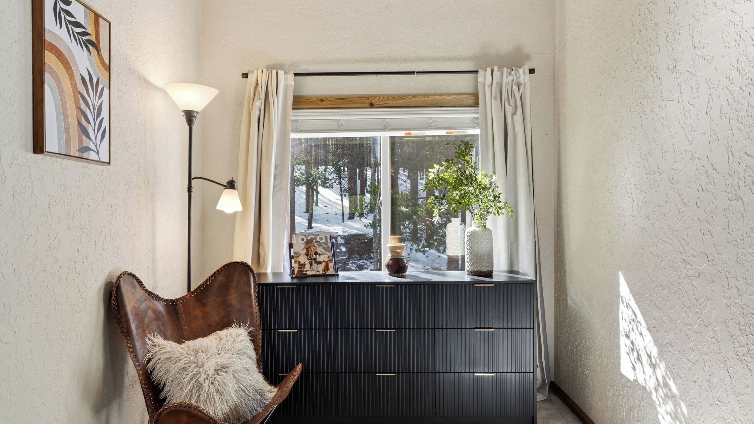 A room with a window, a chair, a lamp, and a dresser.