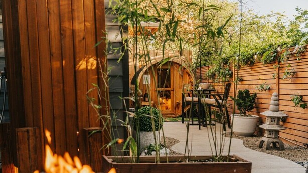 Eine Holzterrasse mit Feuerstelle, Sitzgelegenheiten im Freien und einem Gartenbereich mit Pflanzen und einer Steinhlaterne.