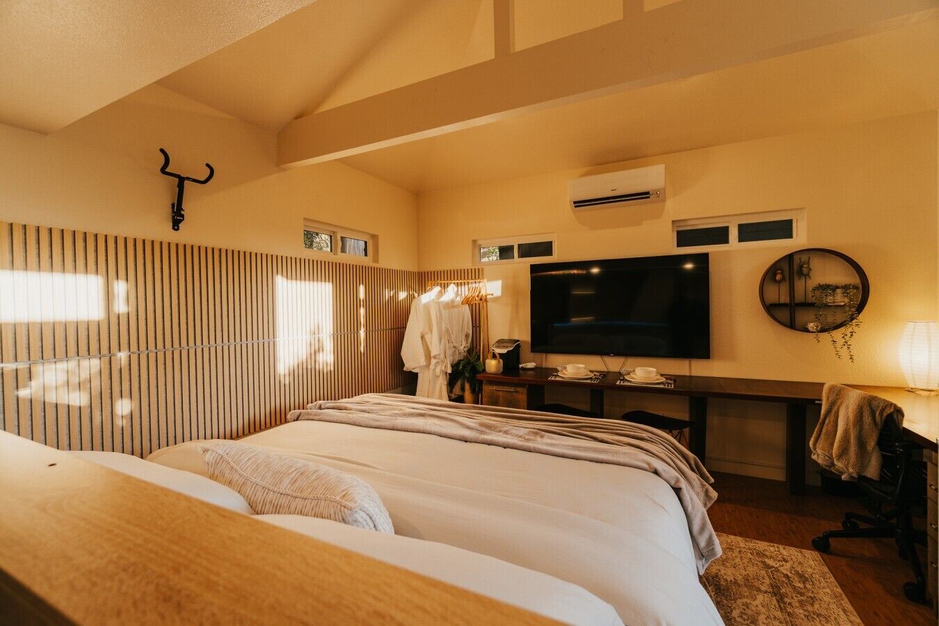 Habitación de hotel con una cama grande, televisión, escritorio con silla y espejo en la pared.