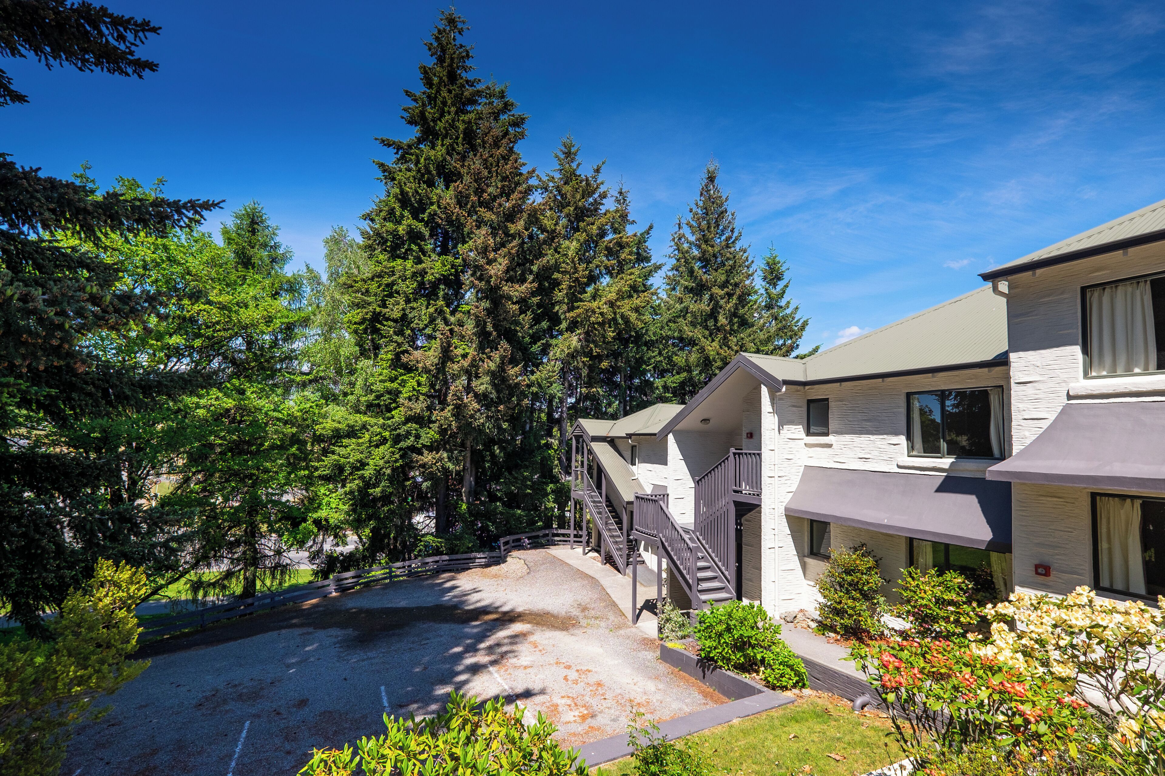A modern two-story building with a covered driveway, surrounded by dense trees and a clear sky.