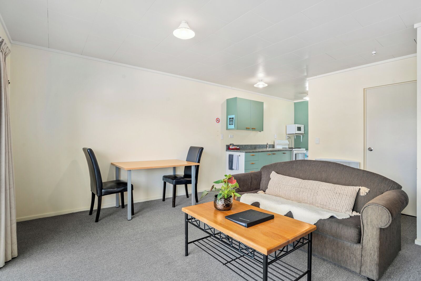 Un espace de vie compact comprenant un canapé, une table à manger avec des chaises, un petit coin cuisine et un luminaire au plafond.