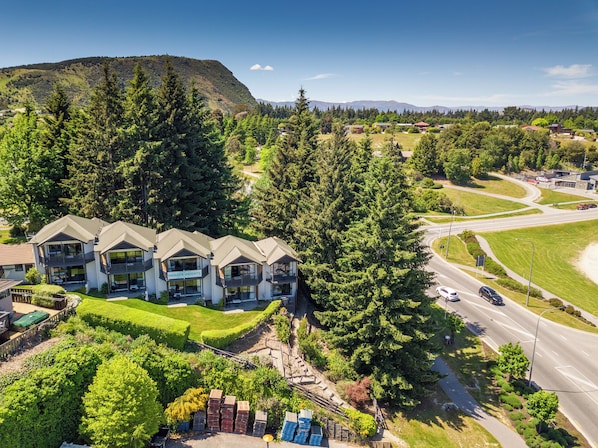 A multi-story hotel with balconies, surrounded by lush greenery and a mountain backdrop.