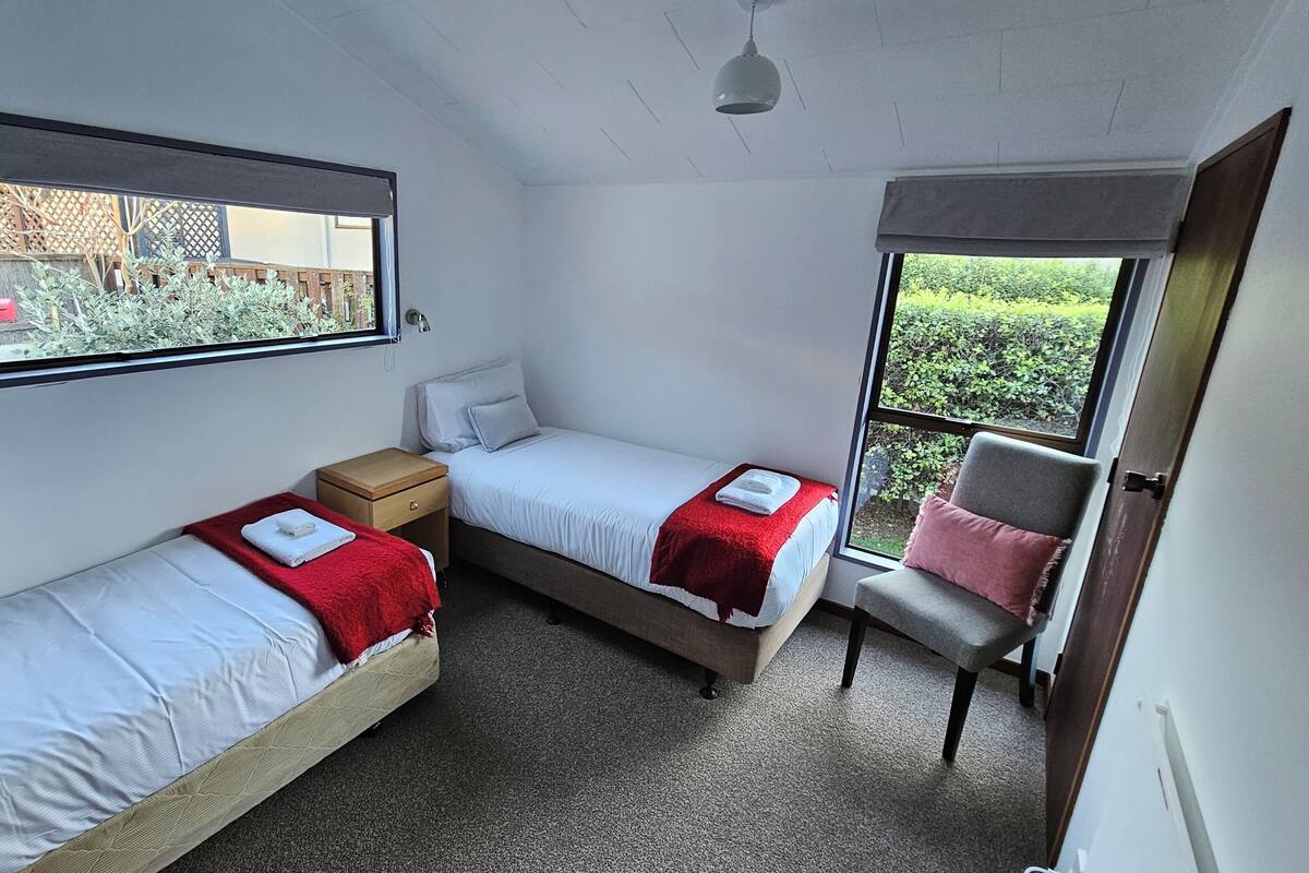 A room with two beds, a window, a chair, and a door.