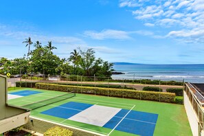 Ein Tennisplatz mit Blick auf den Ozean und Palmen.